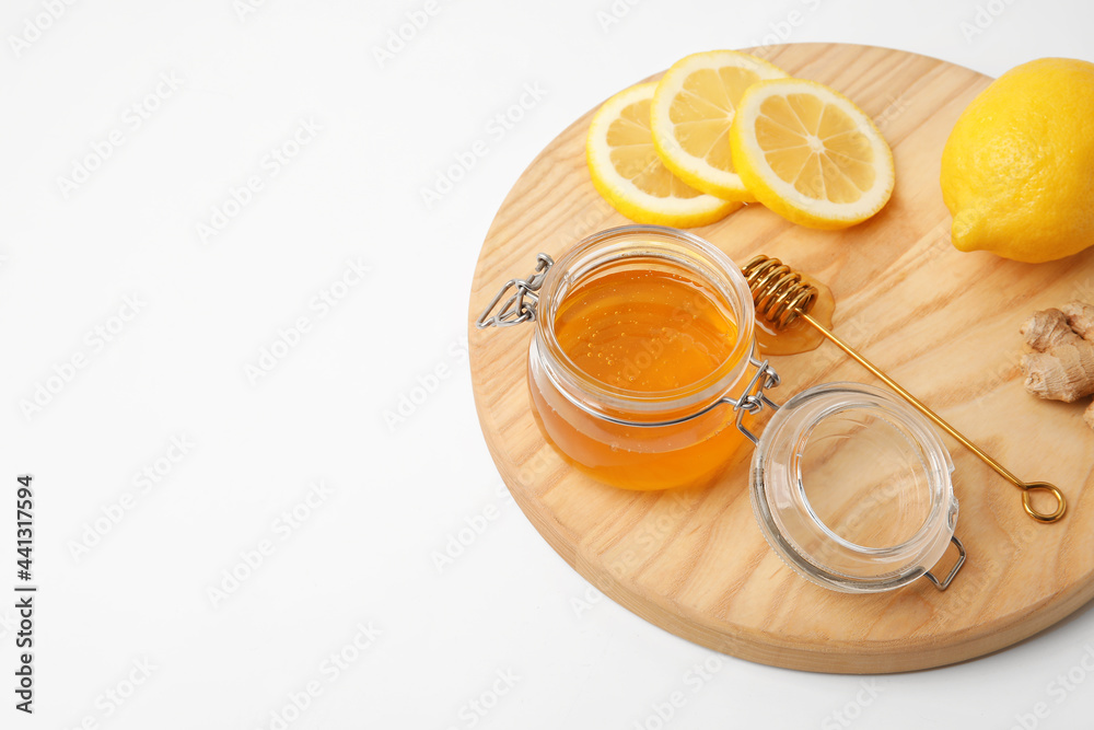 Glass jar with sweet honey, lemon slices and ginger on wooden board against white background