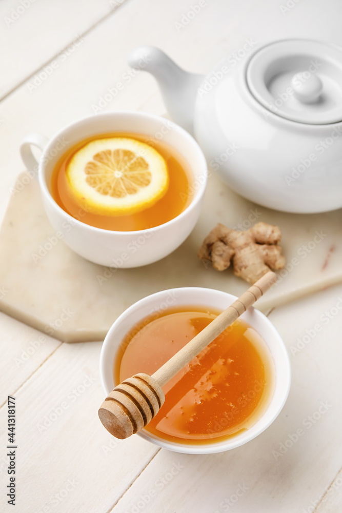 Bowl with sweet honey, teapot, cup of tea and ginger on light wooden background