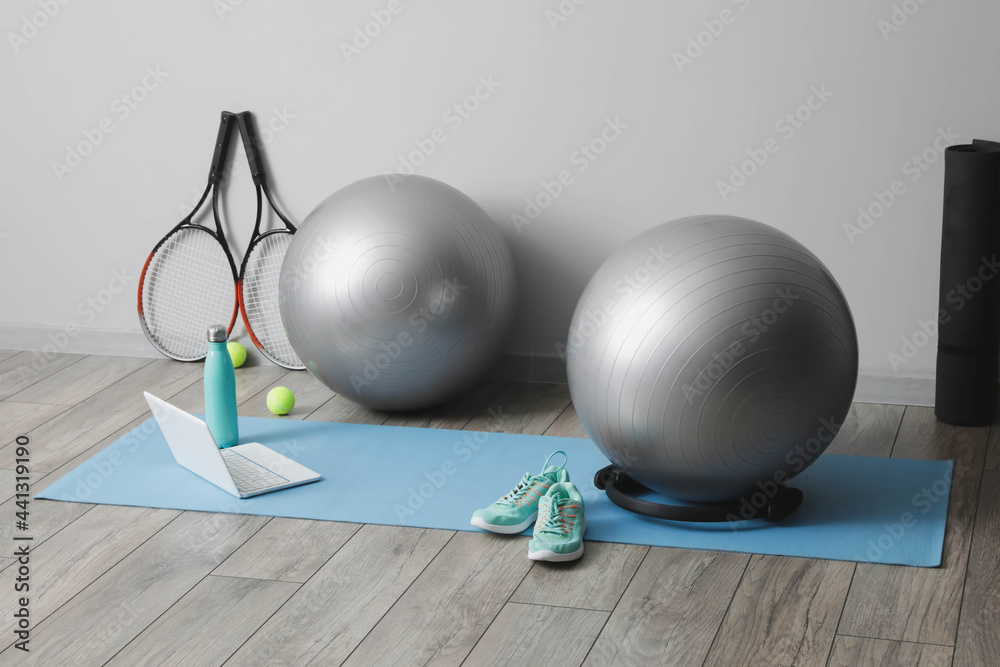 Different sports equipment with fitness balls and modern laptop near light wall