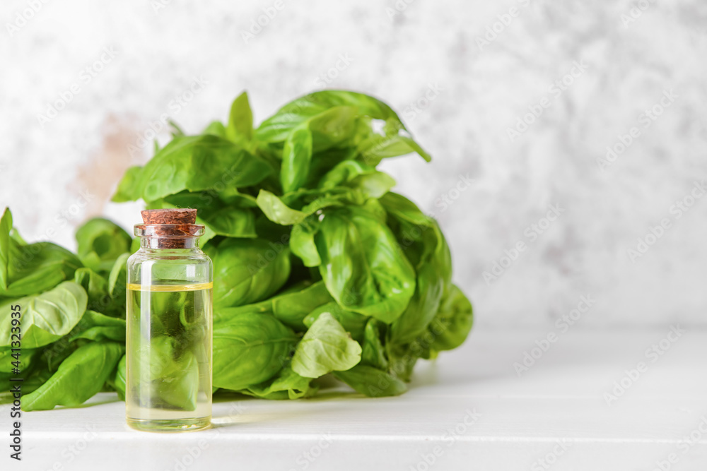 Fresh basil leaves and bottle of essential oil on table