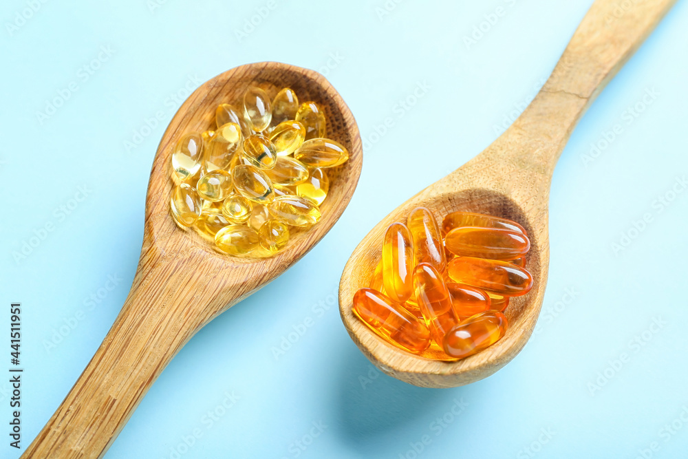 Spoons with fish oil capsules on white background