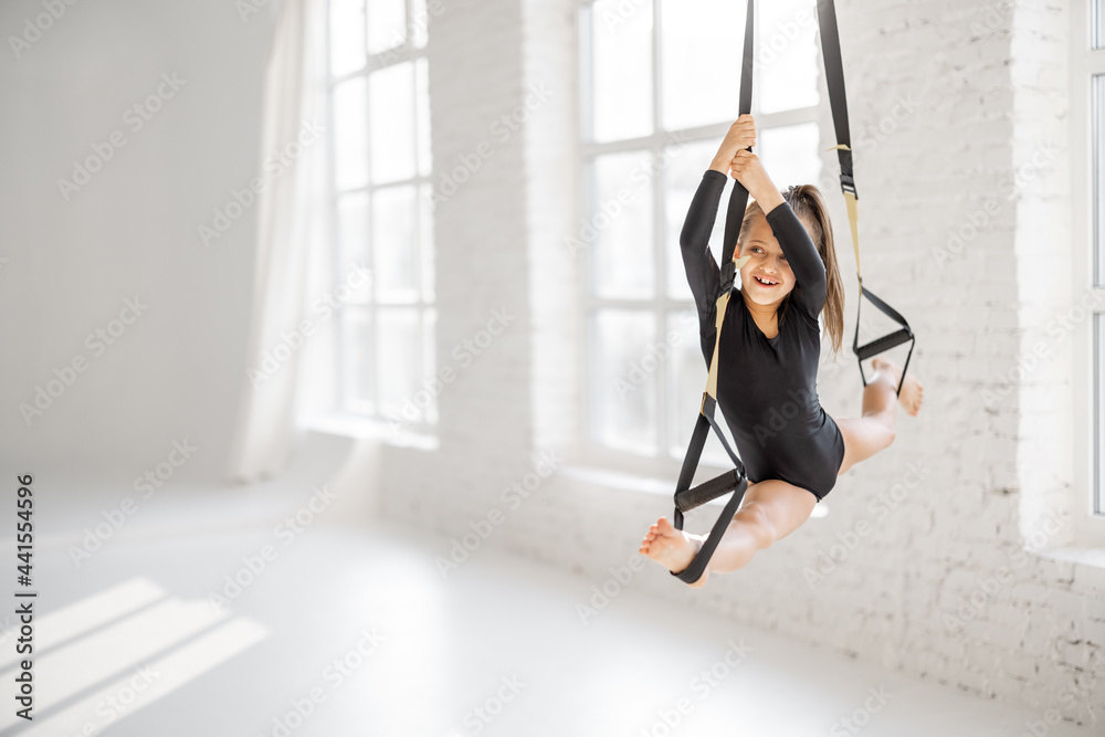 Little girl stretching on suspension straps, doing twine while practicing gymnastics at gym