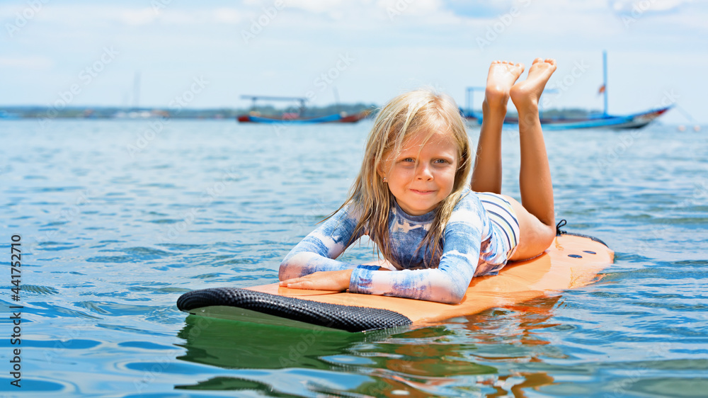 Happy baby girl - young surfer learn to ride on surfboard with fun on sea waves. Active family lifes