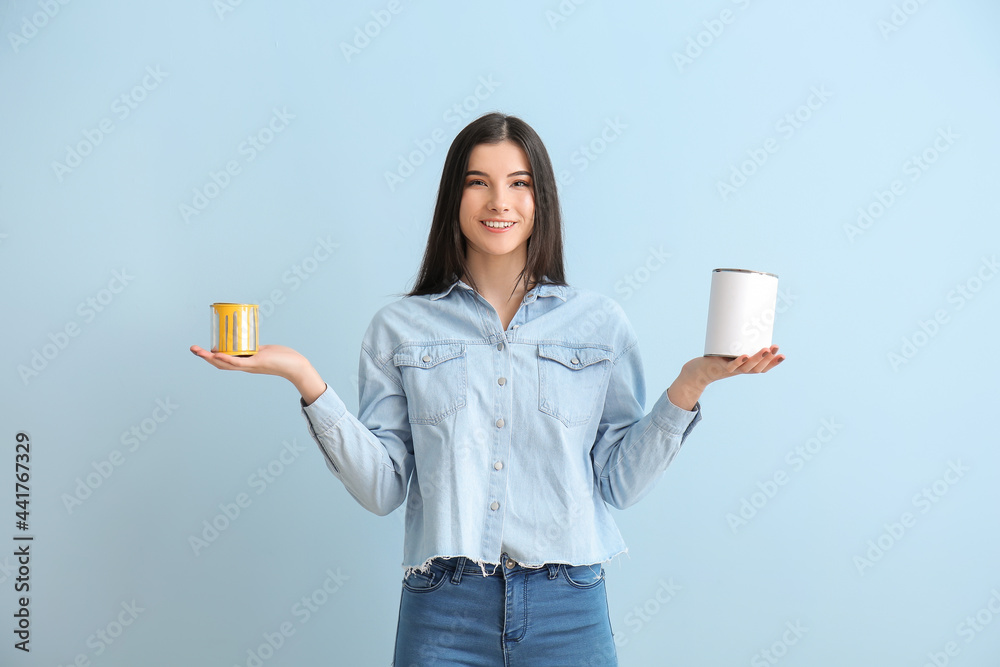 Young woman with cans of paint on color background