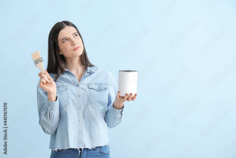 Young woman with brush and can of paint on color background