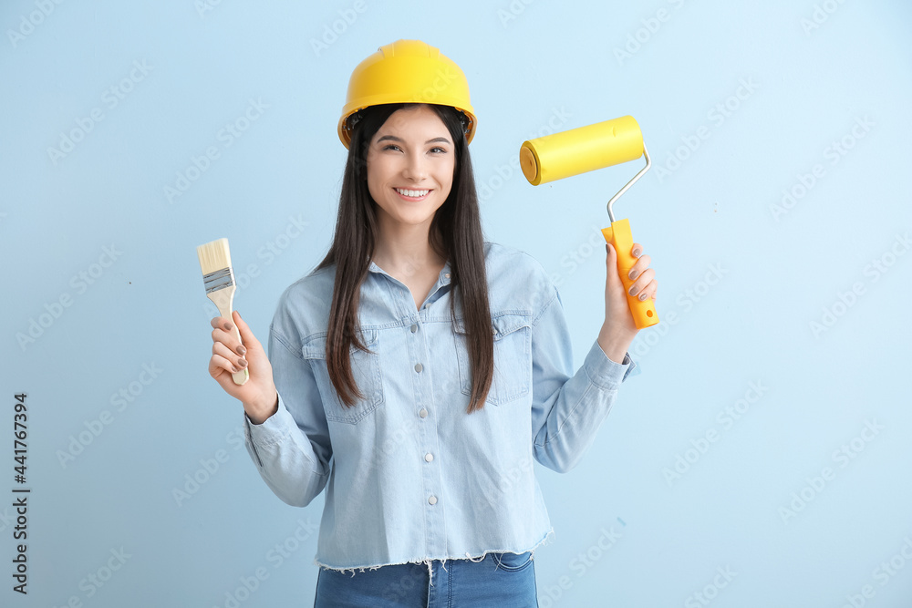 Young woman with brush and paint roller on color background