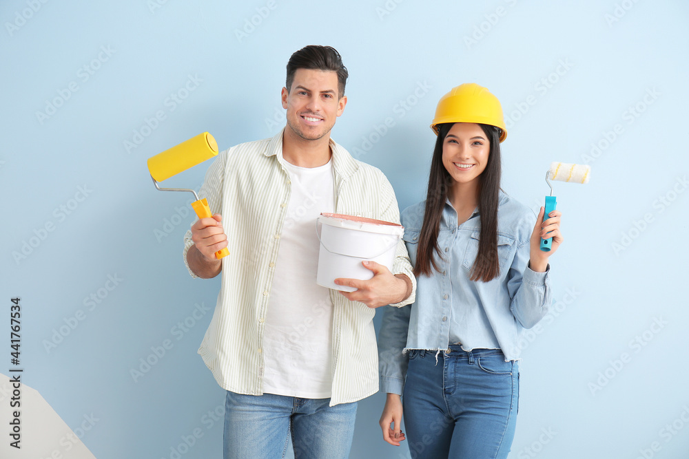 Young couple with rollers and bucket of paint on color background