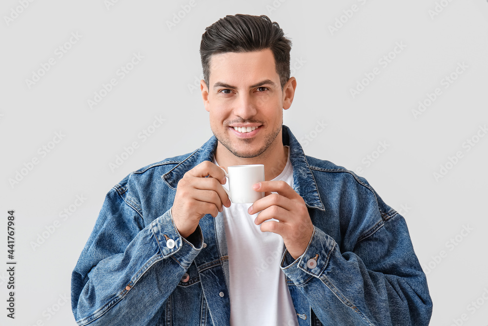 Handsome young man drinking coffee on light background