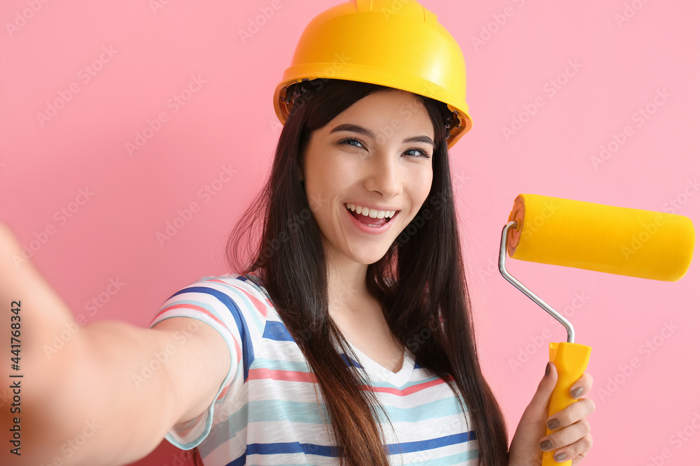 Young woman with paint roller taking selfie on color background