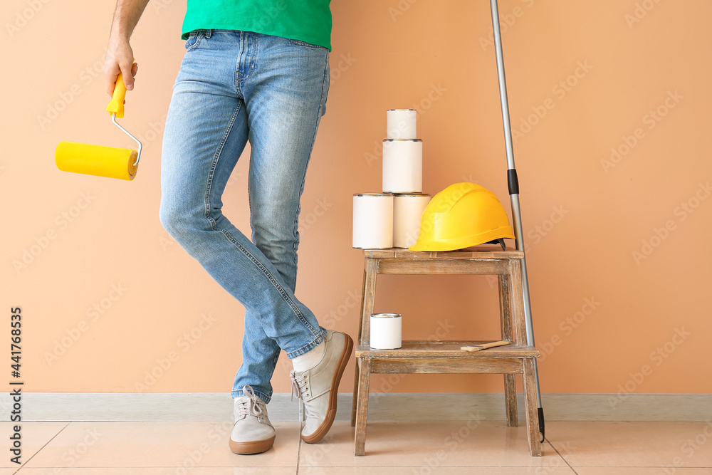 Young man with roller and cans of paint near color wall