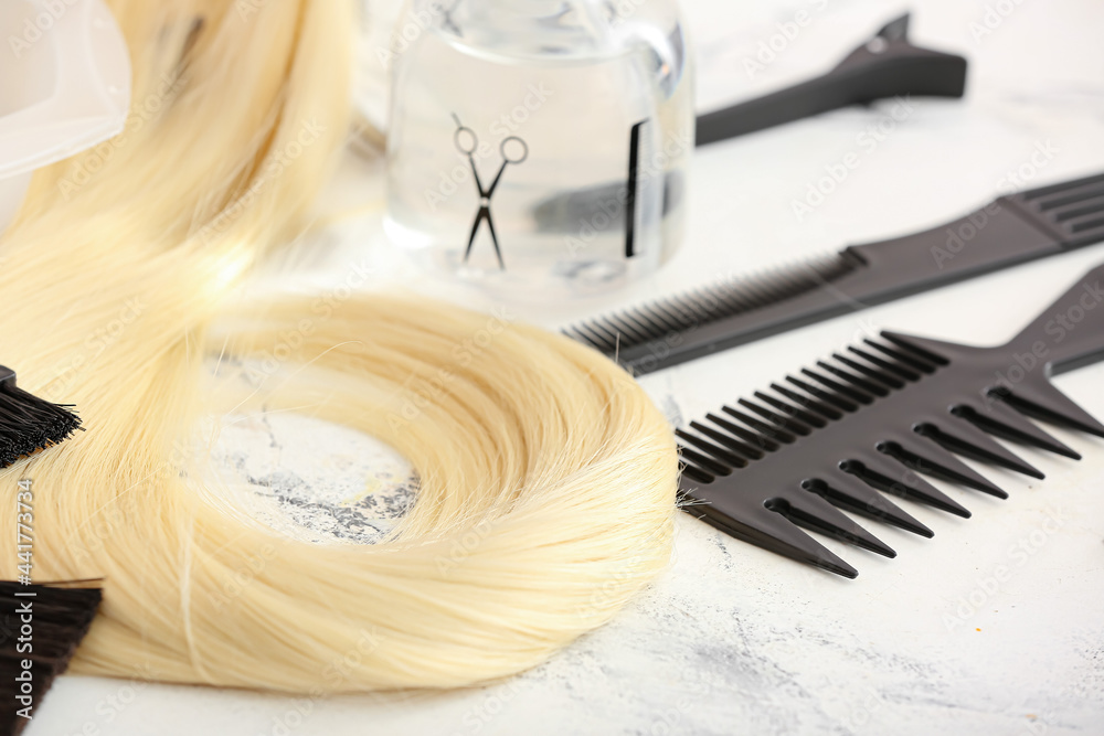 Barbers tools and strand of blonde hair on light background, closeup