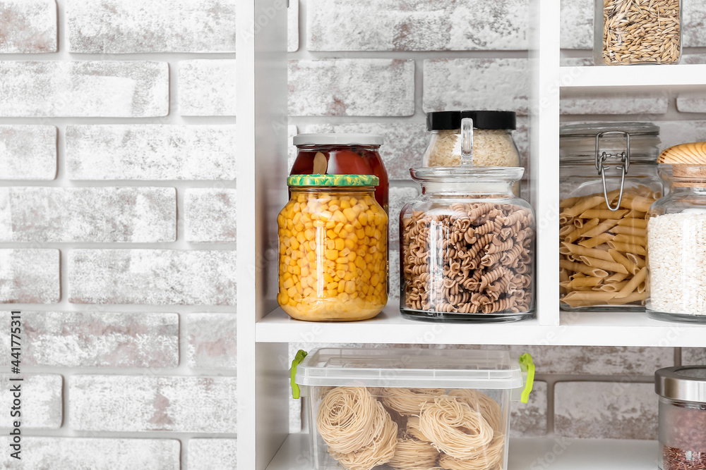 Jars and container with different products on shelves near brick wall