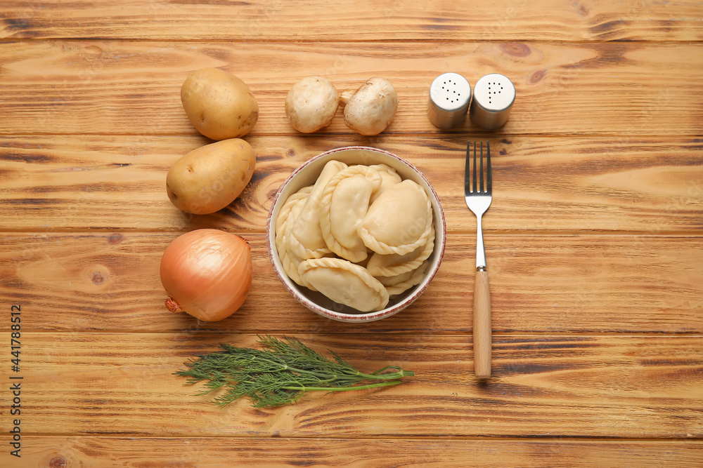 Bowl with tasty dumplings and fresh ingredients on wooden background