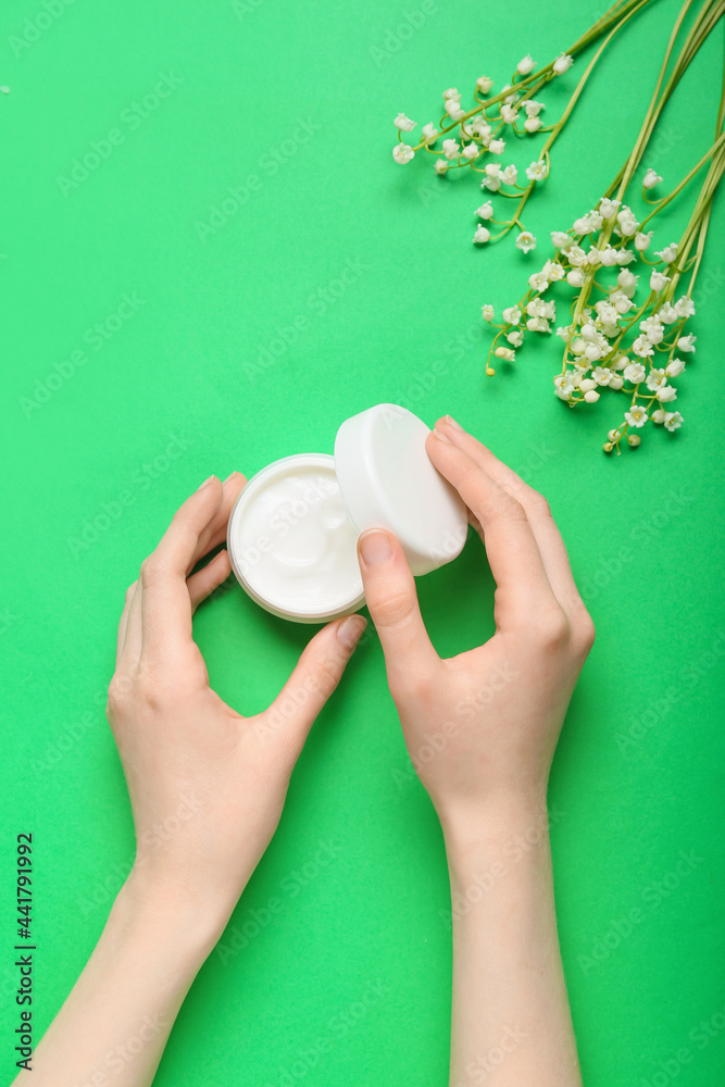 Female hands, jar of cream and lily-of-the-valley flowers on color background