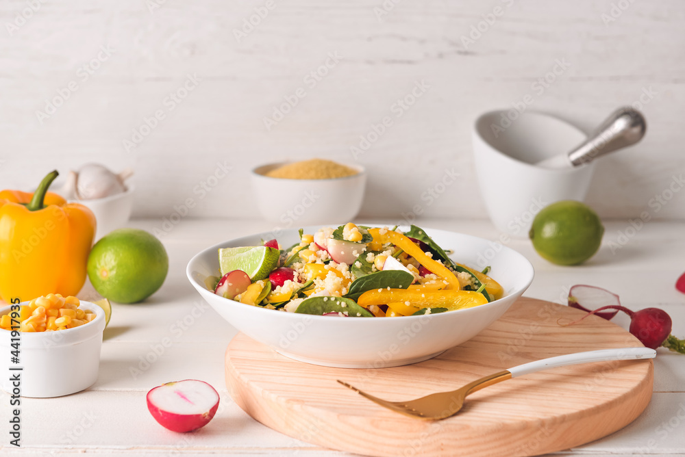 Bowl with couscous and vegetables on light wooden background