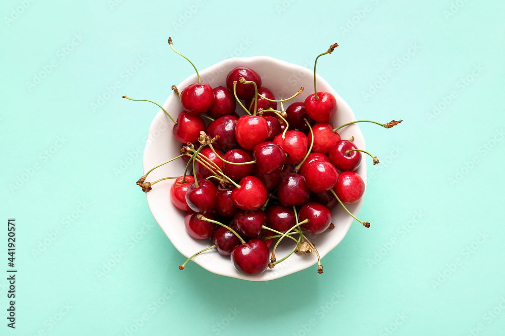 Bowl with tasty ripe cherry on color background