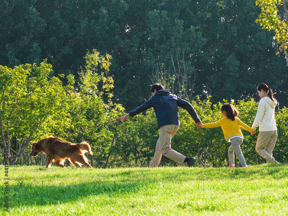 Happy family of three and pet dog walking in the park