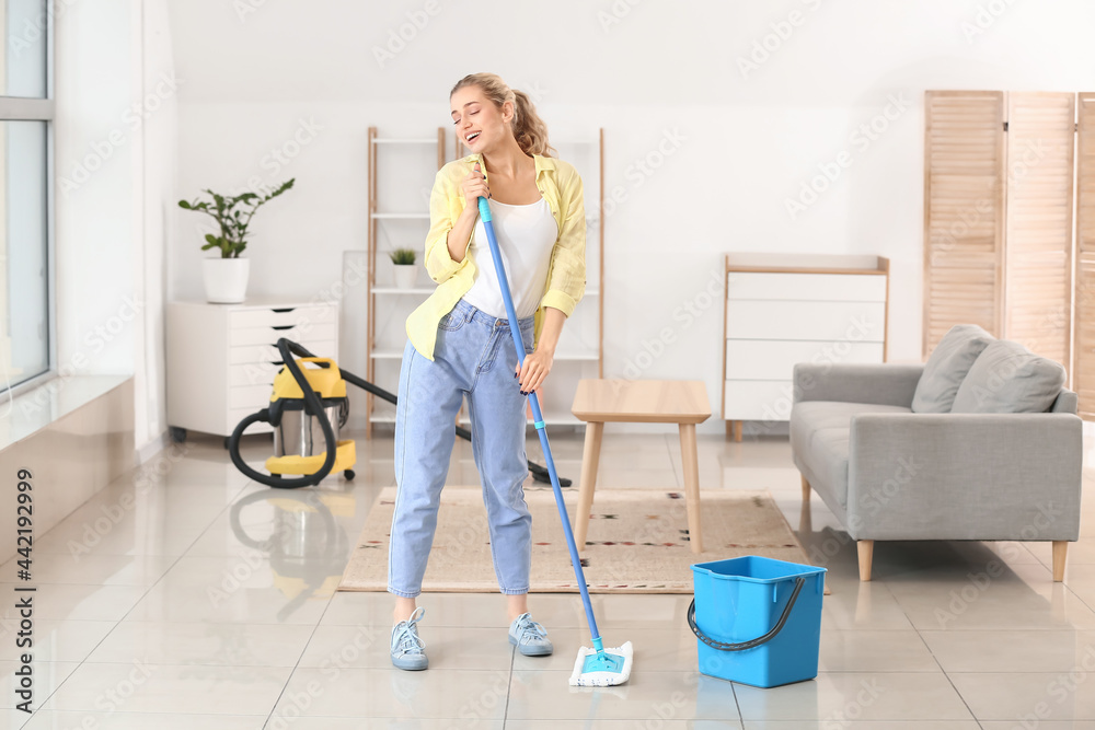 Young woman having fun while mopping floor in her flat