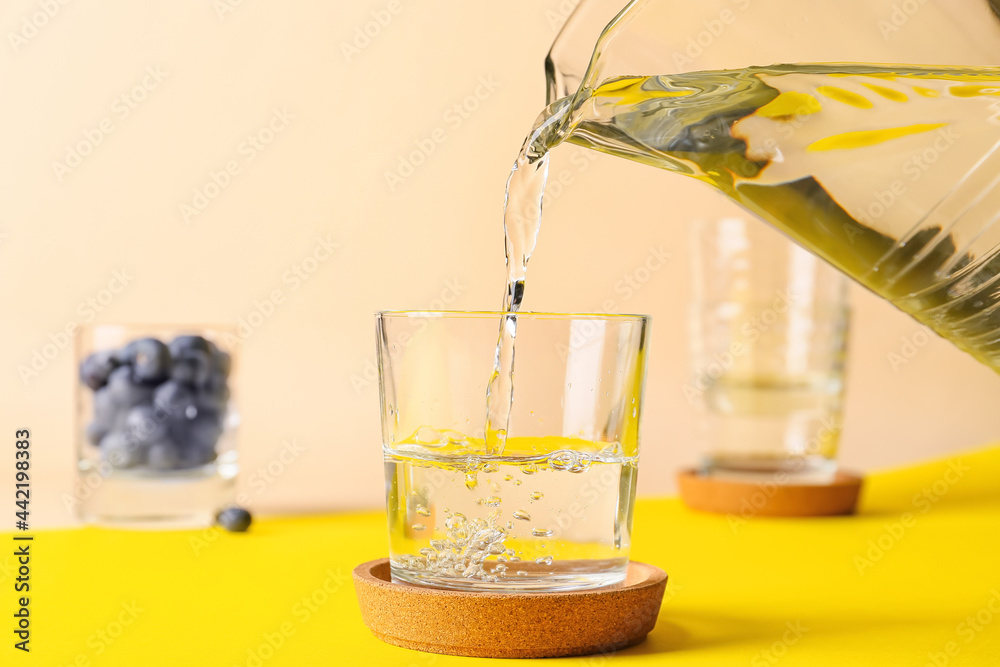 Pouring of water into glass on color background