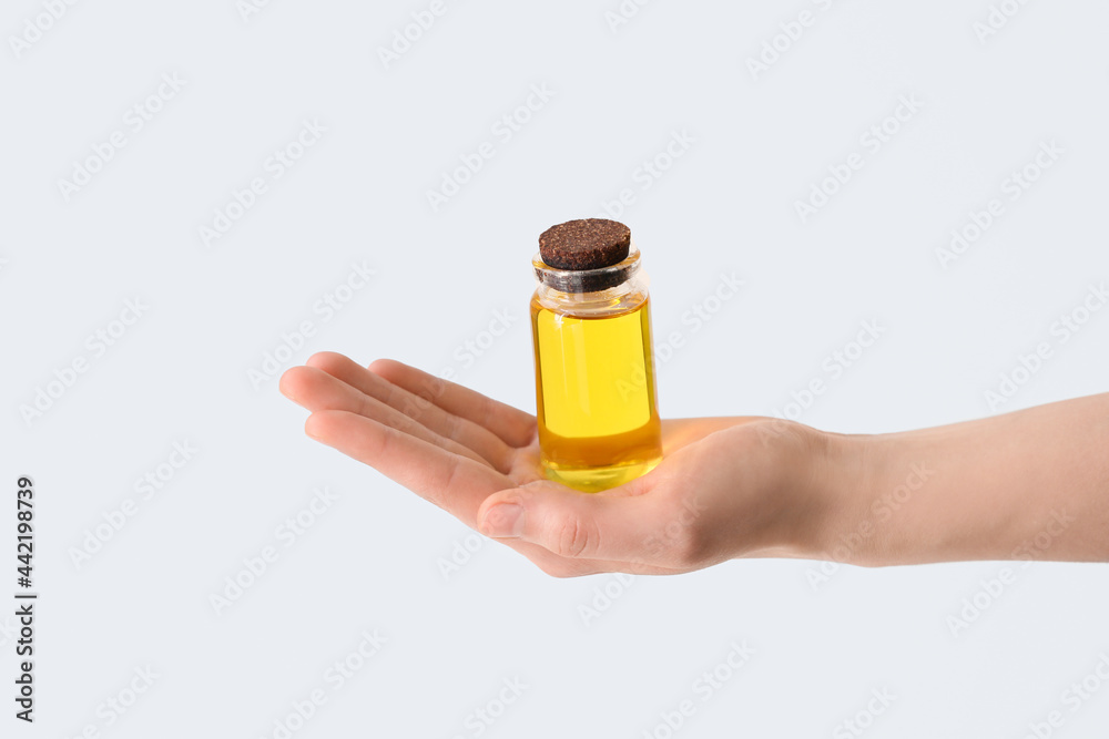 Woman holding bottle of essential oil on light background, closeup