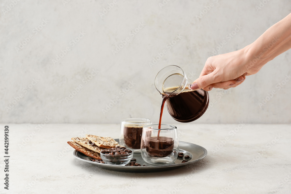 Woman pouring coffee from pot into cup on light background