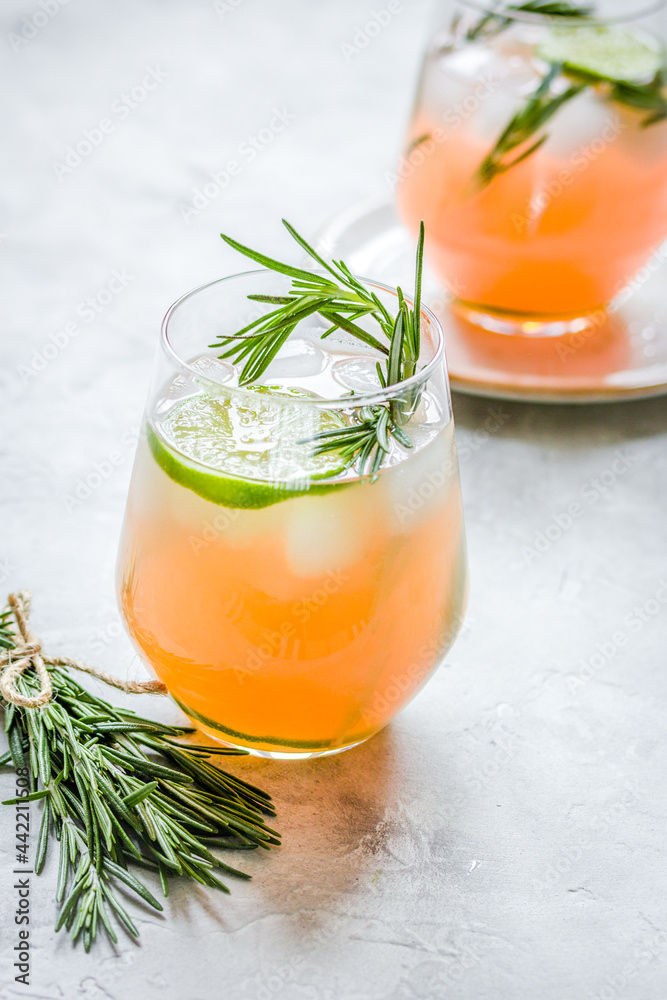 sliced lime, rosemary and natural juice in glass on stone table background