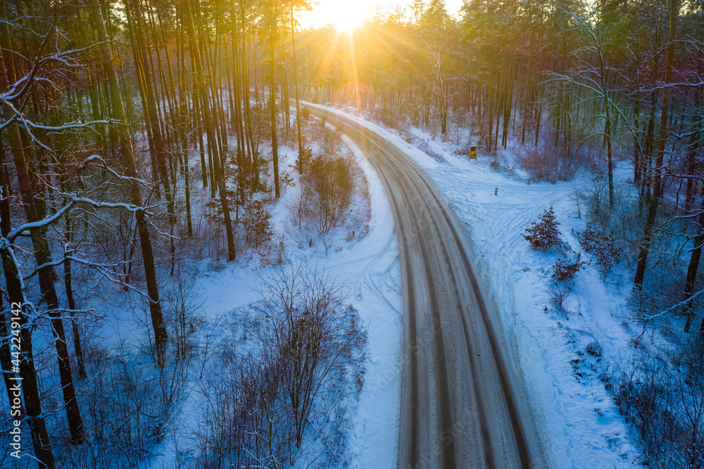 日落时雪林中央冬季道路鸟瞰图