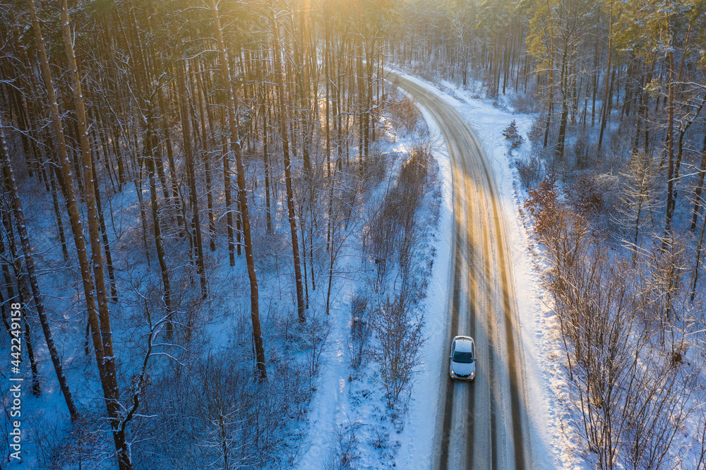 日落时分，雪林中央一条冬季道路的鸟瞰图，汽车在其间行驶