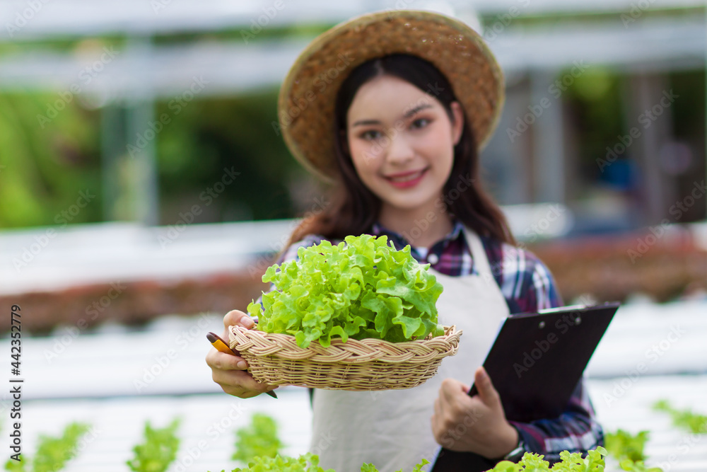 A female farmer inspecting vegetable production in a greenhouse holds a basket of vegetables.