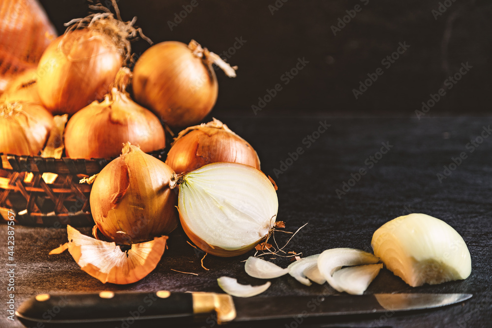 Cebollas y rodajas sobre tabla de cortar de madera y cesto de mimbre. Fondo de alimentos saludables.