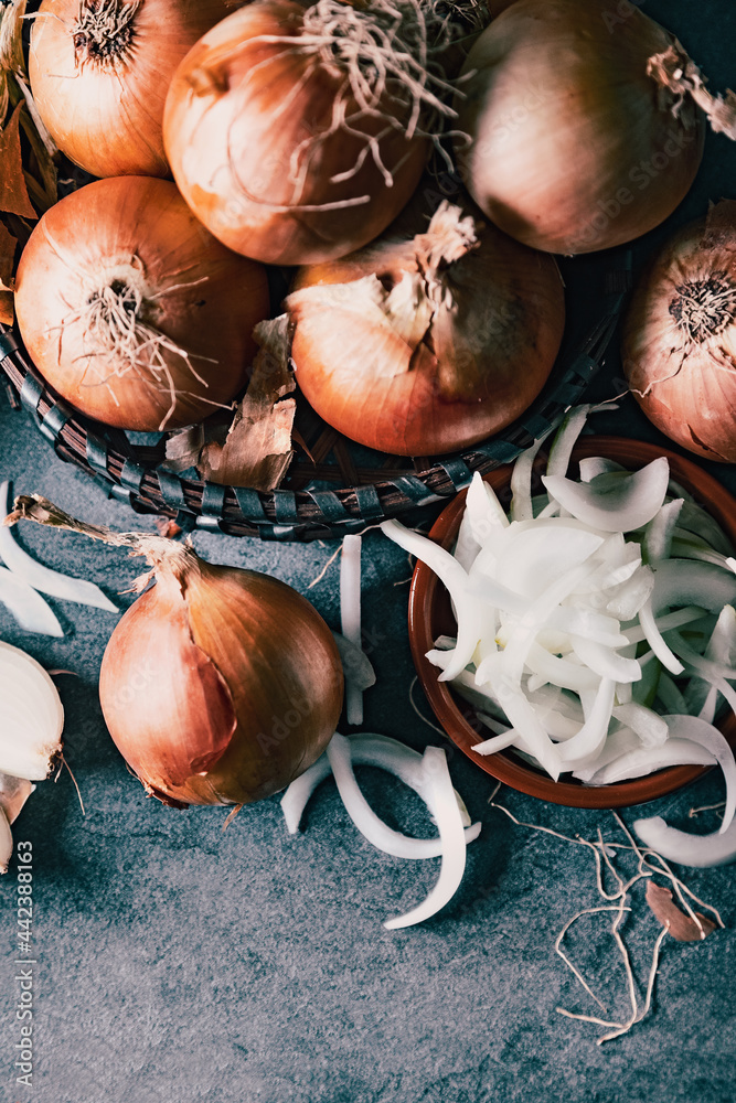 Cebollas y rodajas sobre tabla de cortar de madera y cesto de mimbre. Fondo de alimentos saludables.