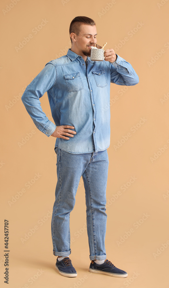 Handsome man drinking hot cocoa on color background