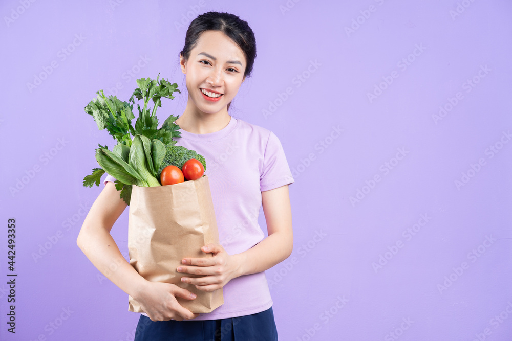 年轻的亚洲女人拿着一袋紫色背景的蔬菜