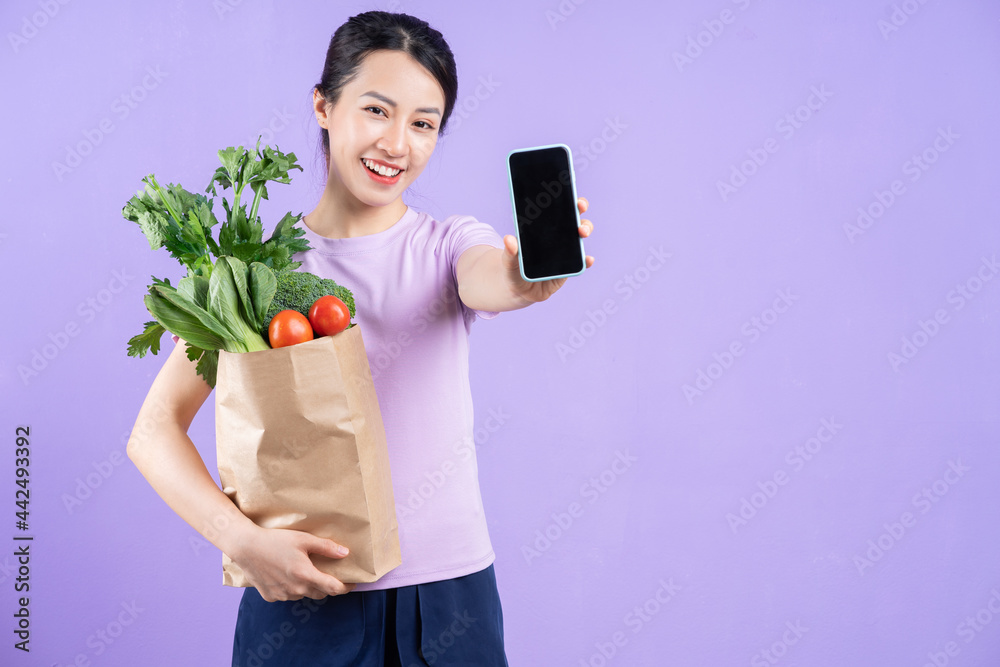 Young Asian woman holding a bag of vegetables on purple background