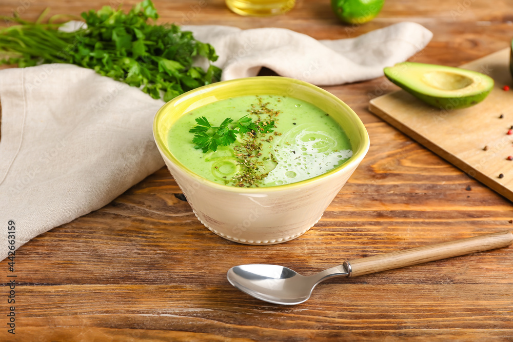 Bowl with green gazpacho and ingredients on wooden background