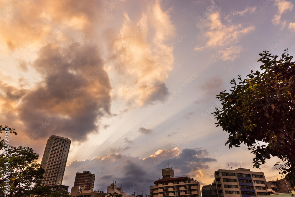 雲の隙間から見える夕暮れの太陽の光と都会のビル