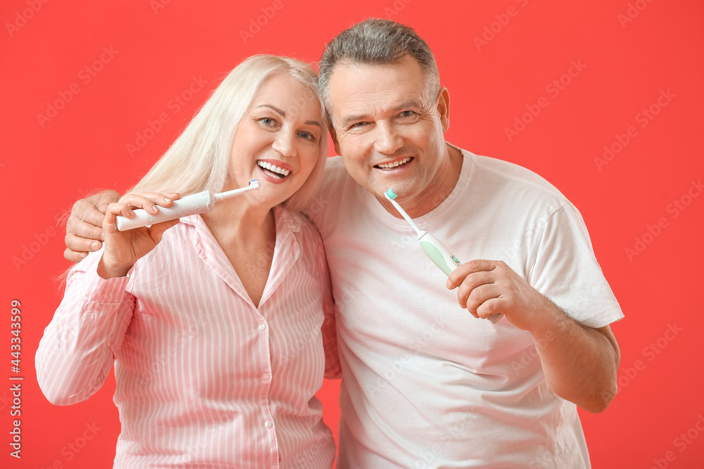 Mature couple brushing teeth on color background