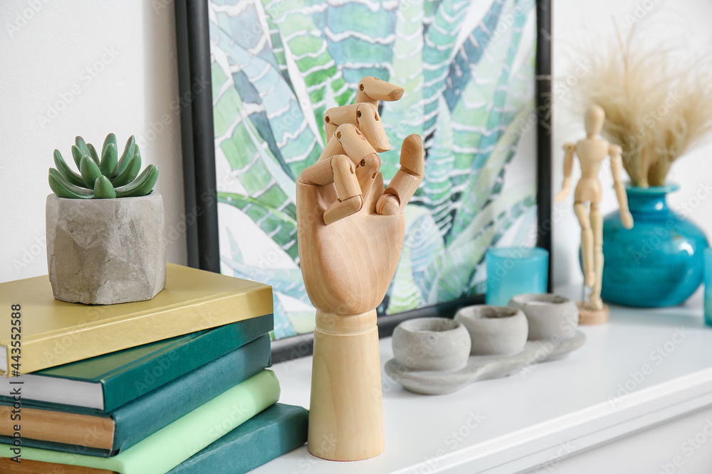 Shelf with wooden hand and books near white wall in room