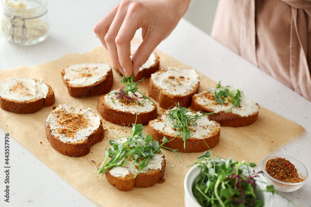 Female chef adding greens to toasts on kitchen table, closeup