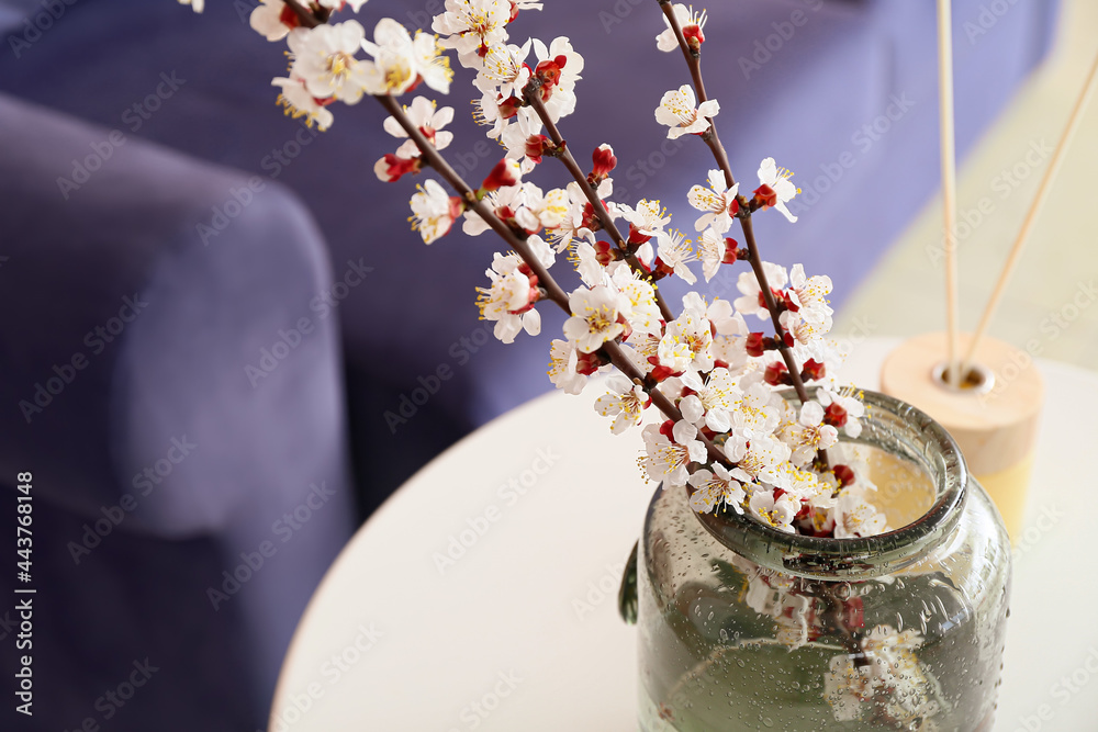 Vase with blooming spring branches on table in room