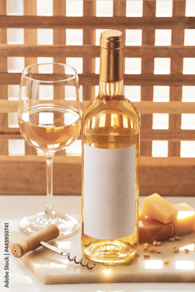 Bottle and glass of exquisite wine, board with cheese and corkscrew on light table