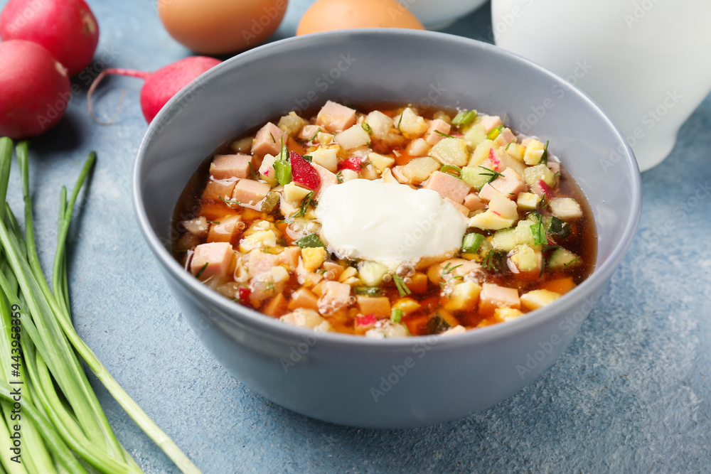 Bowl with tasty okroshka and ingredients on color background