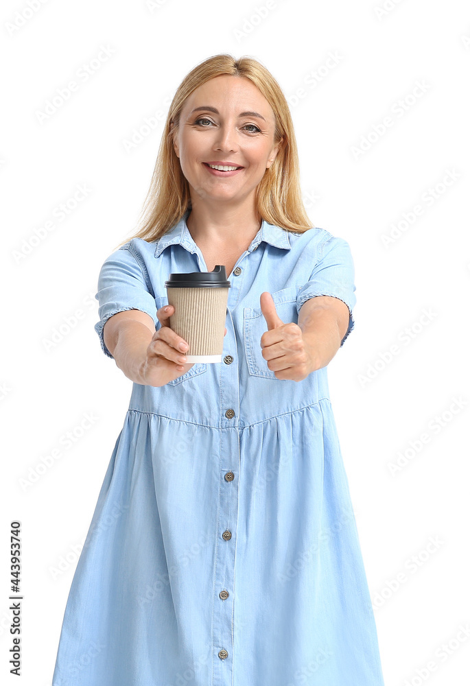 Beautiful mature woman with cup of coffee showing thumb-up on light background