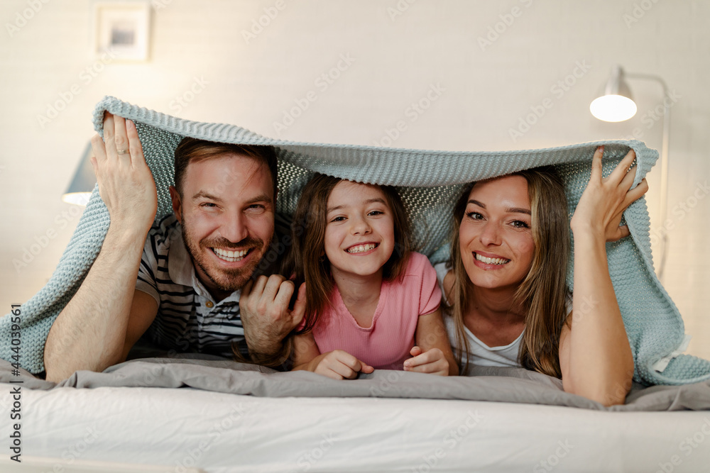 Happy family mother, father and daughter laughing, playing and smiling in bed in bedroom at home.