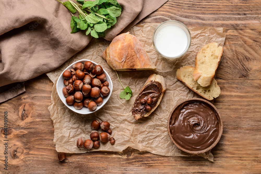 Bowl with tasty chocolate paste and hazelnuts on wooden background