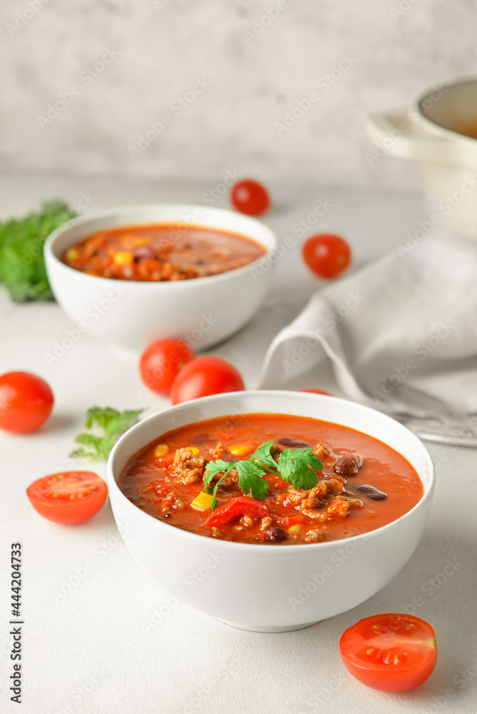 Bowls with delicious chili con carne on light background