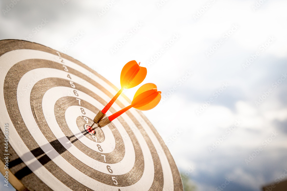 Close up shot red darts arrows in the target  of dartboard center on dark blue sky background. Busin