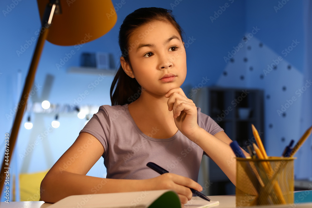 Thoughtful little girl doing homework at home late in evening