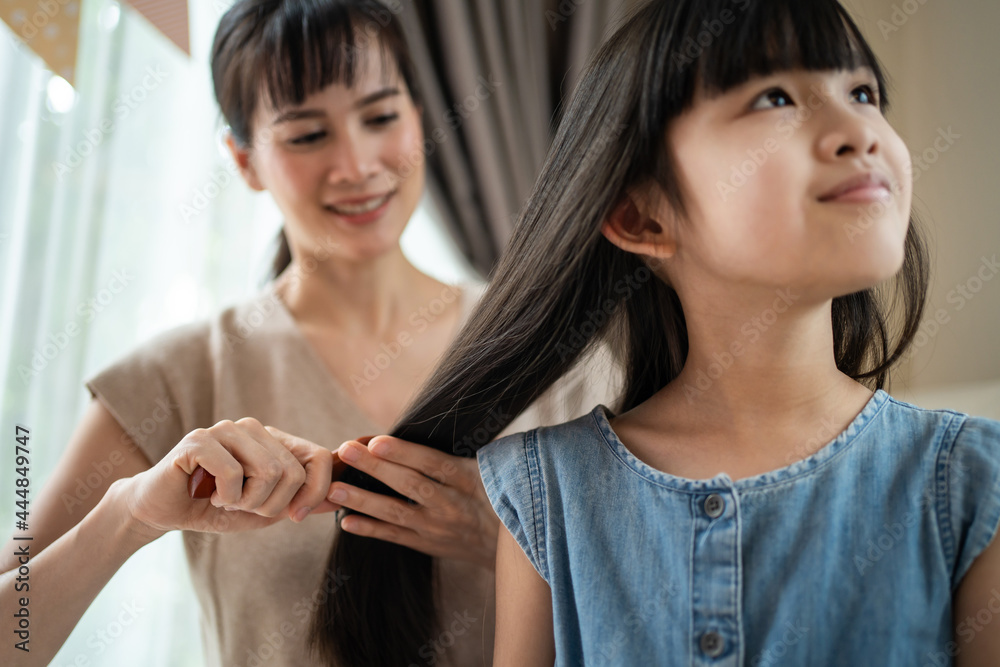 Asian mother combing little kid daughters hair with hairbrush at home