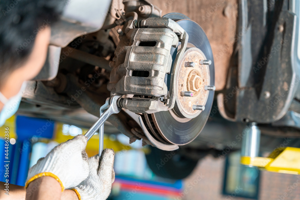 Car mechanic checking a disc brake of the vehicle for repair, in process of new tire replacement. Ca